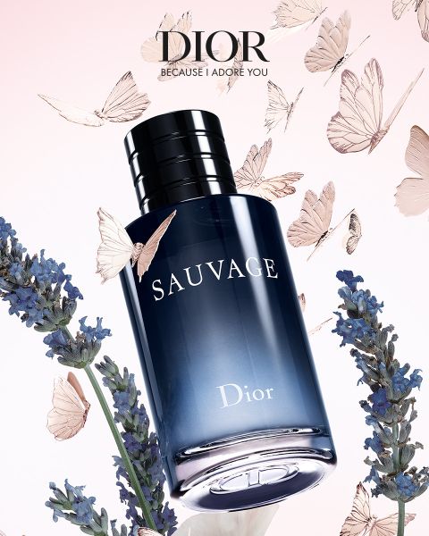 Ein Flakon des Parfums Dior Sauvage ist umgeben von Lavendelblüten und fliegenden Schmetterlingen auf einem Hintergrund mit sanftem rosa Farbverlauf.