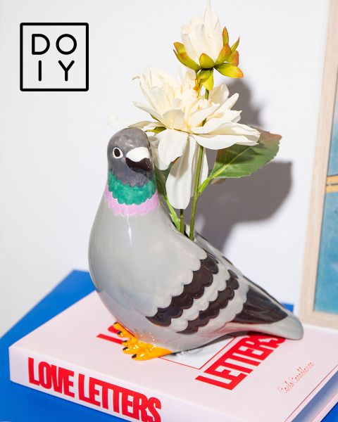 Keramische Taubenvase mit weißen Blumen auf einem "Love Letters"-Buch, mit einem DOIY-Logo in der oberen linken Ecke.
