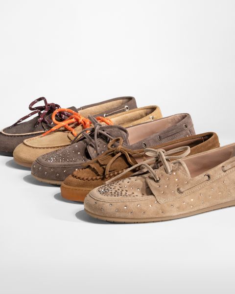 Fünf Paar Mokassin-Slipper aus Wildleder in verschiedenen Farbtönen, einige mit Nieten und bunten Schnürsenkeln, in einer Reihe auf weißem Hintergrund angeordnet.