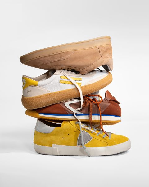 Vier verschiedenfarbige Turnschuhe - hellbraun, weiß, braun und gelb - sind vor einem einfarbig weißen Hintergrund übereinander gestapelt.