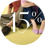 Zwei Personen sitzen mit gekreuzten Beinen auf einem gelben Boden, über dem ein großes "-15%" steht. Einer trägt Halbschuhe, der andere rosa spitze Schuhe.
