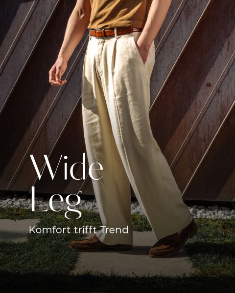Eine Person in einer cremefarbenen Hose mit weitem Bein, braunem Gürtel und braunen Schuhen steht im Freien; der Text lautet "Wide Leg - Komfort trifft Trend".