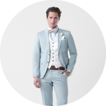 Mann im hellblauen Anzug mit weißer Weste, rosa Fliege und Ansteckblume vor einem schlichten hellen Hintergrund.