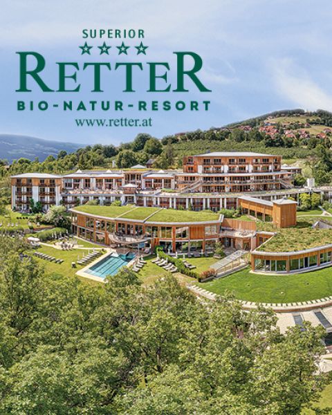 Luftaufnahme des Retter Bio-Natur-Resorts, eines modernen umweltfreundlichen Hotels inmitten von Grünflächen und Hügeln, mit dem Logo und der Website des Resorts darüber.