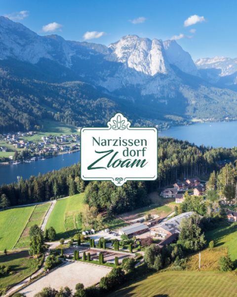 Ein malerisches Alpendorf an einem See mit Bergen im Hintergrund; Textüberlagerung: "Narzissendorf Zloam.