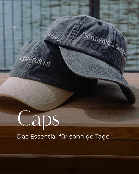 Zwei Baseballmützen mit gesticktem Text sind auf einer Holzfläche gestapelt. Der Text lautet: "Caps - Das Essential für sonnige Tage.