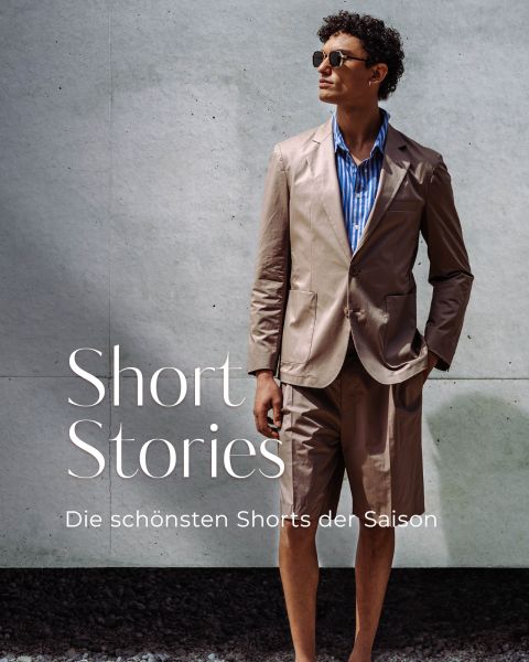 Ein Mann mit Sonnenbrille trägt eine hellbraune Anzugsjacke und passende Shorts über einem blau gestreiften Hemd. Der Text lautet: "Kurzgeschichten. Die schönsten Shorts der Saison.
