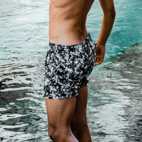 Eine Person, die im flachen Wasser steht und eine schwarz-weiße Camouflage-Badehose trägt, wobei ihr Oberkörper nicht im Bild ist.