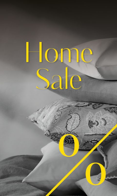 Ein Stapel Kissen in verschiedenen Mustern und Texturen mit der Aufschrift „Home Sale“ und einem großen Prozentzeichen in gelber Schrift.