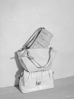 Drei stilvolle Handtaschen in hellen Farbtönen stehen auf einer Holzfläche vor einer schlichten, hellen Wand und sind in einem minimalistischen Ambiente ordentlich angeordnet.