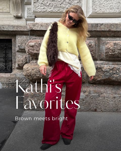 Eine Frau in roten Hosen, einem gelben Pullover und einer Sonnenbrille steht auf einem Bürgersteig und lächelt. Der Text lautet: „Kathis Favoriten. Braun trifft auf Knallfarben.“.