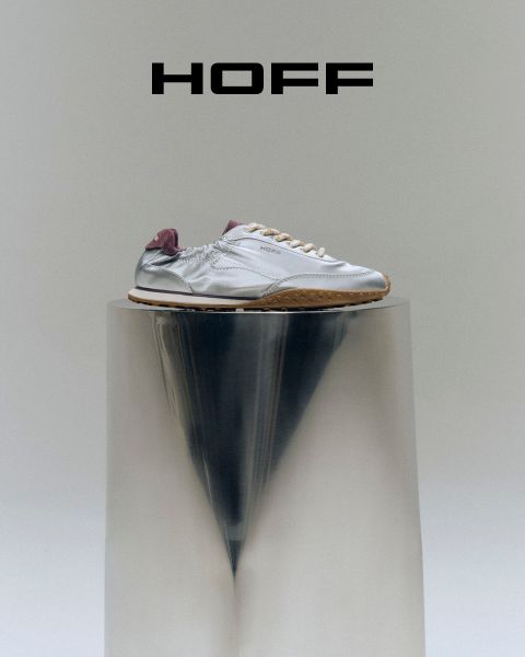 Ein silberner Turnschuh mit violettem Absatz steht auf einem reflektierenden Sockel unter dem „HOFF“-Logo auf hellgrauem Hintergrund.