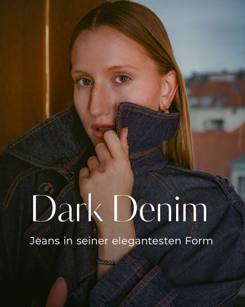 Eine Person in einer dunklen Jeansjacke posiert in einem Innenraum, den Kragen hochgeschlagen, überlagert von den Schriftzügen „Dark Denim“ und „Jeans in seiner elegantesten Form“.