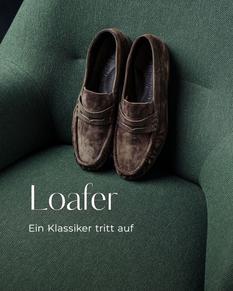 Ein Paar braune Wildleder-Loafer liegt auf einem grünen Stoffsessel. Der Text lautet: „Loafer. Ein Klassiker tritt auf.“.