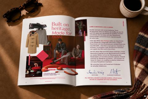 Ein aufgeschlagenes Magazin mit Modeartikeln, ein Brief auf Deutsch, eine Sonnenbrille und ein karierter Schal auf einer braunen Unterlage.