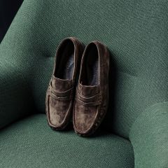 Ein Paar braune Wildleder-Loafer, die auf einem strukturierten grünen Sessel liegen.