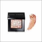 Ein Highlighter-Puder von Bobbi Brown mit gewebtem Muster und einem Farbmuster aus schimmerndem Puder daneben auf weißem Hintergrund.