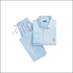 Ein hellblaues Pyjamahemd mit Knöpfen und eine dazu passende Hose mit Kordelzug, beides ordentlich zusammengefaltet, mit einem kleinen dunklen Logo auf der Hemdtasche.