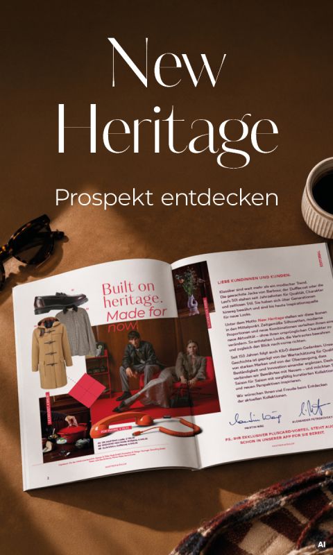 Ein aufgeschlagenes Magazin auf einer braunen Fläche, darüber der Schriftzug „New Heritage Prospekt entdecken“ sowie eine Sonnenbrille und eine Tasse daneben.