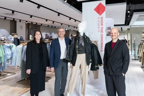 Four adults stand in a clothing store beside a mannequin wearing layered outerwear and a scarf, smiling at the camera.