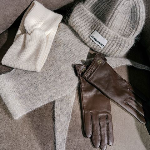 Ein cremefarbenes Strickstirnband, eine graue Strickmütze von Armedangels, ein passender grauer Schal und ein Paar braune Lederhandschuhe.