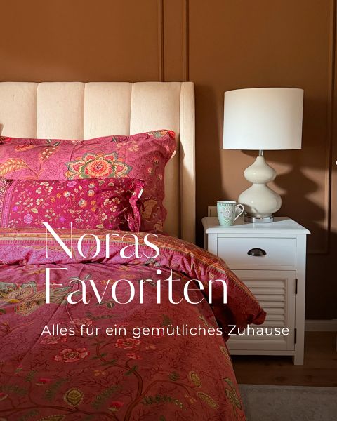 Ein Bett mit rosa Bettwäsche mit Blumenmuster, ein weißer Nachttisch mit einer Lampe und einer Tasse sowie der Schriftzug „Noras Favoriten: Alles für ein gemütliches Zuhause“.