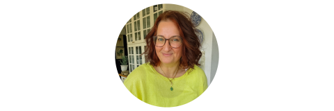 Eine Frau mit schulterlangen rotbraunen Haaren und Brille, die ein leuchtend gelbes Oberteil trägt.