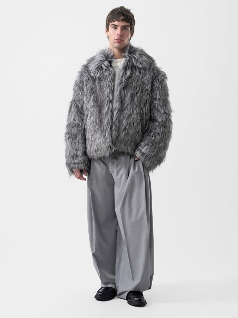 Ein Mann, der eine graue Kunstfelljacke, einen cremefarbenen Pullover und eine graue Hose mit weitem Bein trägt.